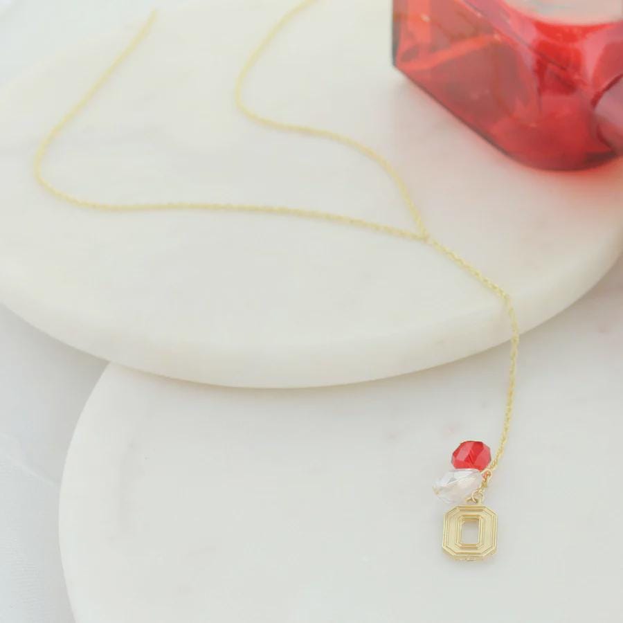 Gold Y necklace with crystal charm, pearl bead and red accent on white background