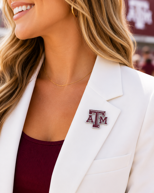 Woman wearing a white blazer and maroon top featuring a Texas A&M crystal logo pin with maroon rhinestone detailing and silver-tone finish.